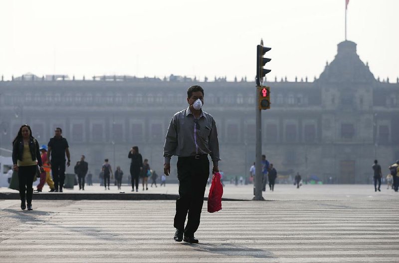 A man wears a face mask Thursday as he walks in Mexico City’s haze-shrouded main square near the National Palace.