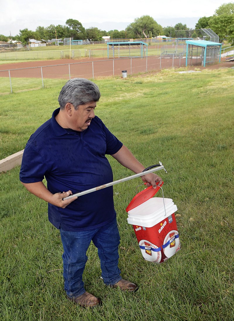 In this May 8, 2019, photo, Hector Aguilar uses a claw grabber extension to remove a hypodermic needle from one of the baseball fields at Atrisco Park, home of the Atrisco Valley Little League, in Albuquerque, N.M. The little league park is fighting a battle against discarded syringes with attached hypodermic needles amid the region&#x2019;s outgoing opioid epidemic. (Jim Thompson/The Albuquerque Journal via AP)