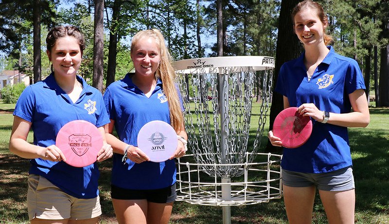 From left, Dani Hunter, Whitney Brown, and Madison Chitwood prepare to practice on the disc golf course at Southern Arkansas University. Chitwood won the women’s individual competition at the National Collegiate Disc Golf Championships on March 29, 2019.