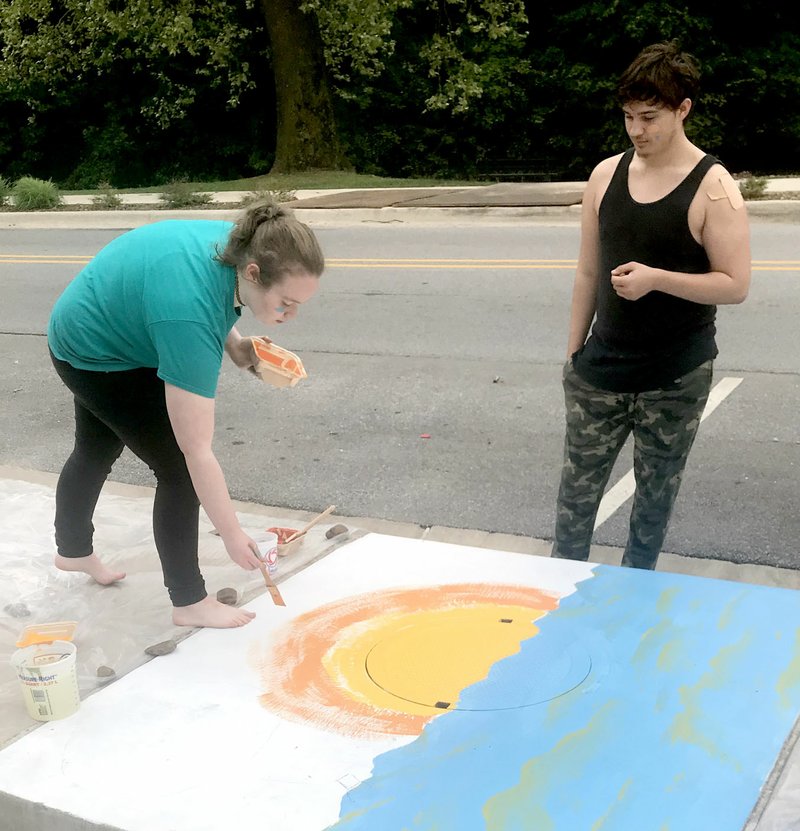 Photo submitted Siloam Springs High School students Dannie Dobson, left, and Cody Bartlett paint storm water drains near downtown Siloam Springs in an effort to bring awareness to keeping the storm drains and creeks litter free.