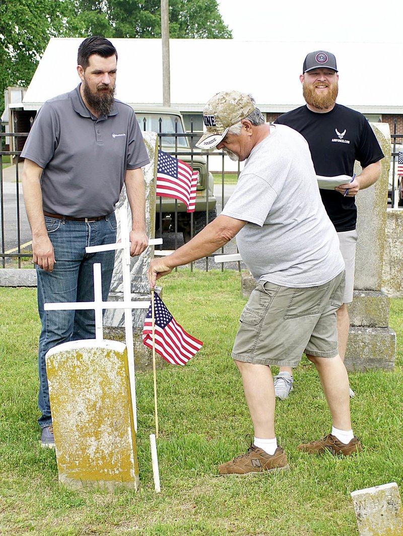 Westside Eagle Observer/RANDY MOLL After Christopher Dale and Matt McClain placed a cross, Jimmy Roberts places a flag on a veteran's grave in Decatur Cemetery on Saturday. Crosses and flags were placed by the Decatur VFW post with assistance from the city of Decatur and WoodmenLife.