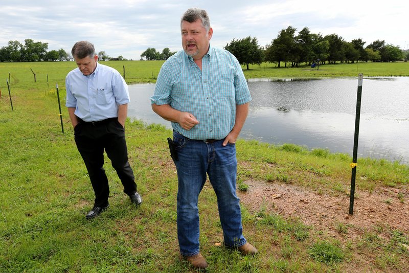 NWA Democrat-Gazette/DAVID GOTTSCHALK Al Drinkwater, consultant, listens Tuesday to Jason Steele with NWA Steele Farms describe the pvc pipe and condition of one of the cattle ponds on the family farm in Bethel Heights. The Steele family says Bethel Heights' Lincoln Street Waste Water Treatment Plant system is polluting water on the property.