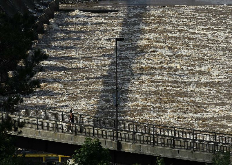 A woman and her dog jog up the ramp of the Big Dam Bridge as the water churns from the dam Wednesday in Little Rock. The Arkansas River is predicted to reach 30-year highs over Memorial Day weekend.  