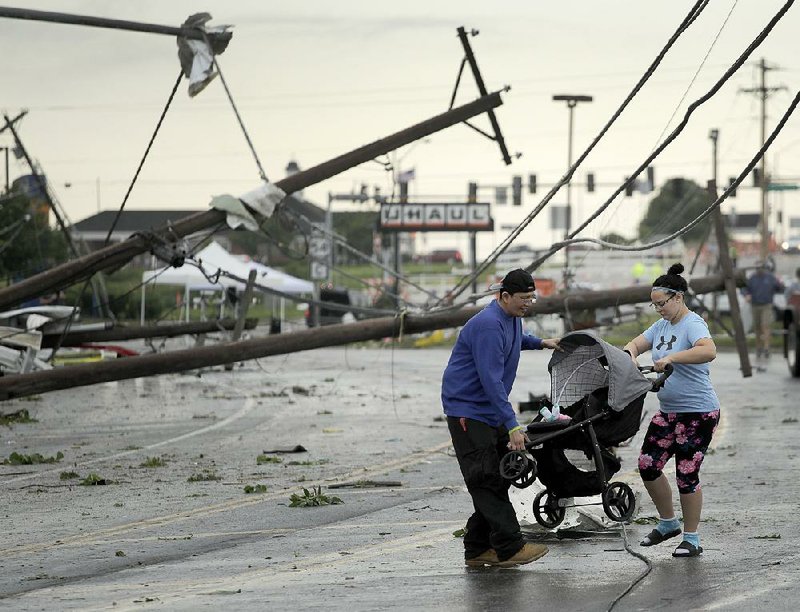 Jessica Rodgers and neighbor Ray Arellana carry a stroller with Rodgers’ sister Sophia Rodgers over downed power lines as they head to Rodgers’ mother’s apartment to check on damage Thursday, after a tornado tore though Jefferson City, Mo. late Wednesday.