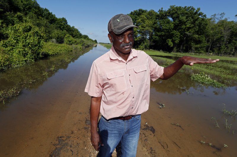 In this Thursday, May 23, 2019 photo, Larry Walls, a farmer and businessman stands at the edge of a backwater flooded road leading to his 560 acres of rented farm land near Louise, Miss. Walls can no longer drive to the property without the possibility of getting flooded or stuck.  (AP Photo/Rogelio V. Solis)