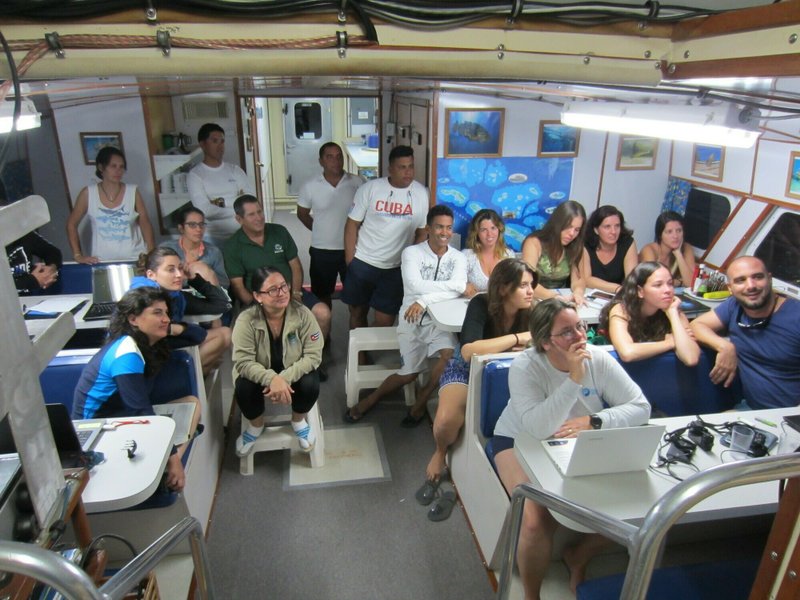 In this Dec. 12, 2018 photo provided by the Environmental Defense Fund, Patricia Gonzalez, director of the University of Havana's Center for Marine Research, third from right, sitting in front of a laptop, attends a field workshop with fellow Cuban scientists, and government officials, aboard a vessel at Parque Nacional Jardines de la Reina, Cuba. The New York-based Environmental Defense Fund has worked with Cuban universities, research centers and the Cuban government for 19 years on marine and coastal conservation. (Environmental Defense Fund via AP)