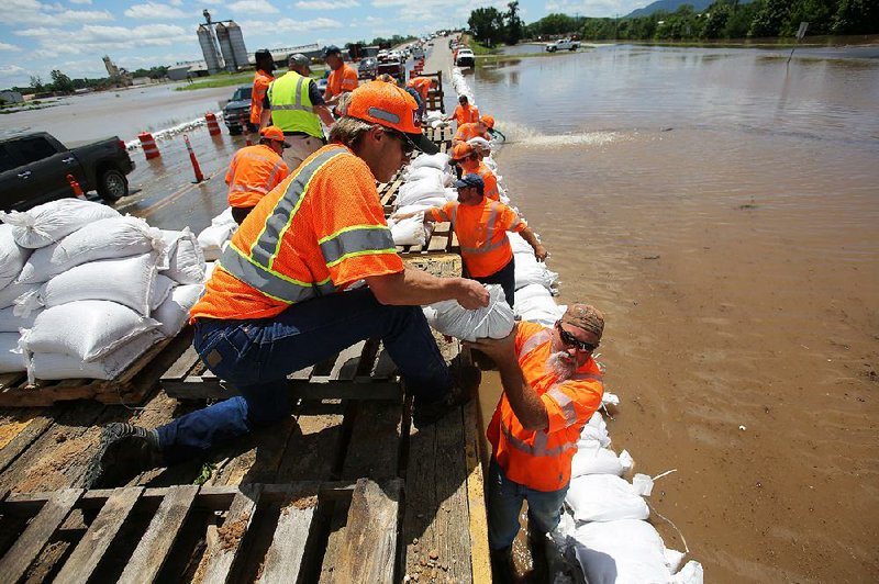 Jacob Loomis (center), Gary Hogrefe and other Arkansas Department of Transportation workers set out sandbags Thursday on the approach to the Arkansas 7 bridge over the Arkansas River at Russellville. 