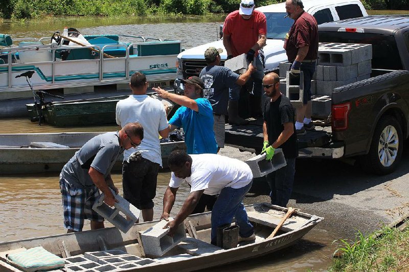 Volunteers from New Life Church in Pine Bluff help load cinder blocks into a boat Friday at Island Harbor Estates for use in raising furniture and appliances off the floors of houses.