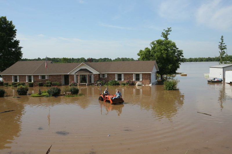 Jud Haley rides on the front of his brother Floyd's tractor through floodwaters after the two had removed some item's from Floyd Haley's home on Sunday, June 2, 2019, on Willow Beach Road in North Little Rock. 