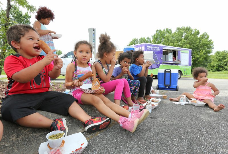 NWA Democrat-Gazette/DAVID GOTTSCHALK Egypt Goings (left), 4, enjoys lunch Monday with neighborhood children provided by the Fayetteville Public Schools' Purple Dog Food Truck at the American Legion post on Curtis Avenue in Fayetteville. The American Legion location is the new third location for the food truck that will provide a lunch to those 18 and younger. Northwest Arkansas school districts begin their free summer food service programs for kids this week.