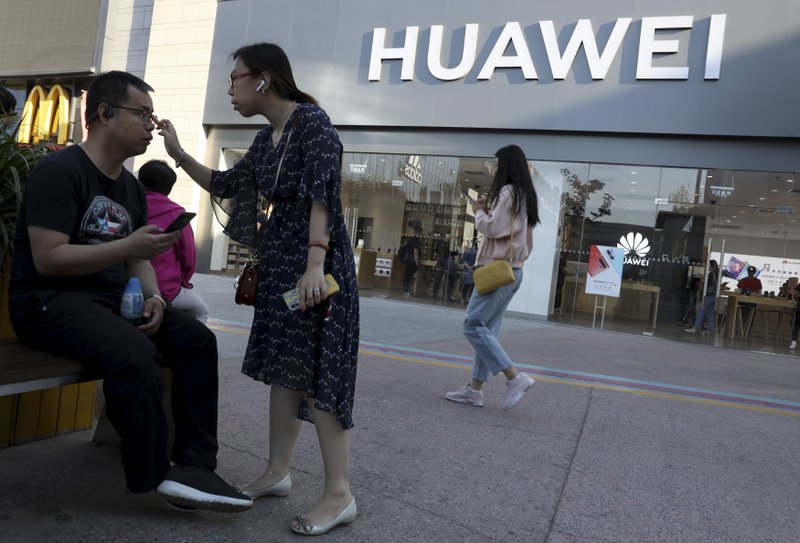 In this May 20, 2019, photo, a woman adjusts the glasses of a man outside a Huawei store in Beijing. The world's largest association of technology professionals has reversed a decision that would have excluded employees of Chinese tech giant Huawei and its affiliates from some editorial and peer review activities.(AP Photo/Ng Han Guan)