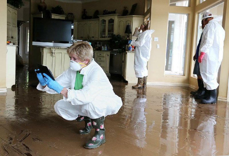 Pat Faubus gets photographs of the water level on the walls of her home Tuesday on Riverview Drive in Fort Smith. Faubus, her husband, Don, and their daughters returned for the first time since May 25, when Arkansas River flooding forced them to leave. 