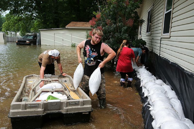 Joseph Shireman heaves a couple of sandbags out of a boat Wednesday while he, Kayla Biggs, Connor Green and others work to protect Shireman’s home on Lake Conway as water continues to rise on the 6,700-acre lake. More photos are available at arkansasonline.com/66flooding/ 