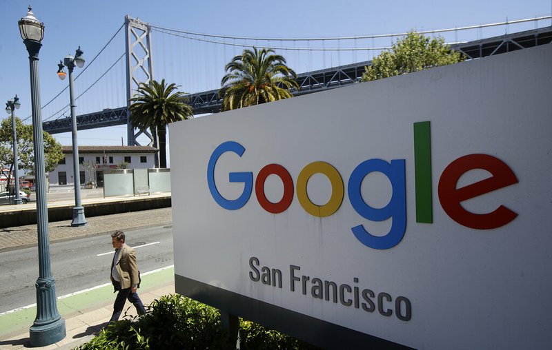 In this May 1, 2019, file photo a man walks past a Google sign outside with a span of the Bay Bridge at rear in San Francisco. Google is acquiring data analytics firm Looker for $2.6 billion cash in an effort to expand its Google Cloud business. The company says Looker will give its cloud-computing customers more ways to use their data. (AP Photo/Jeff Chiu, File)