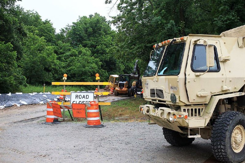 An Arkansas National Guard team stands by Thursday as heavy equipment earth movers work to shore up the levee along Island Harbor Marina Road in Pine Bluff. 