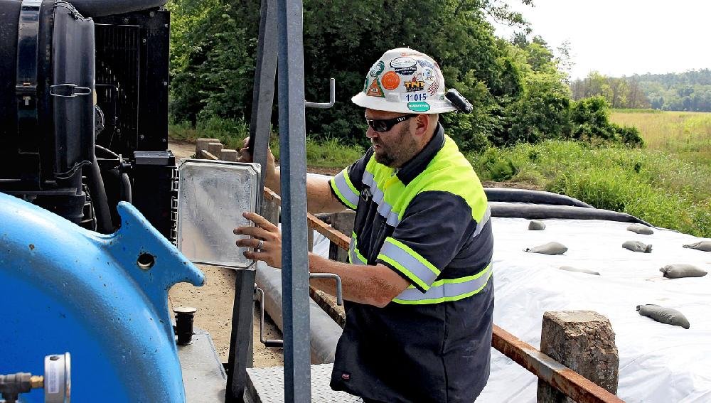 Rain for Rent employee Ryan Frye of Conway checks the readings Saturday on two pumps on a bridge over Tucker Creek as workers pump water from one side of a temporary dam to the other to divert water out of the Conway side of the creek.