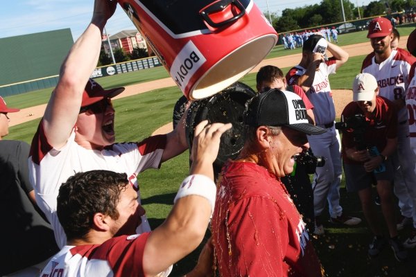 Arkansas players Heston Kjerstad and Dominic Fletcher douse coach Dave Van Horn after defeating Mississippi in Game 3 at an NCAA college baseball super regional tournament Monday, June 10, 2019, in Fayetteville, Ark. (AP Photo/Michael Woods)