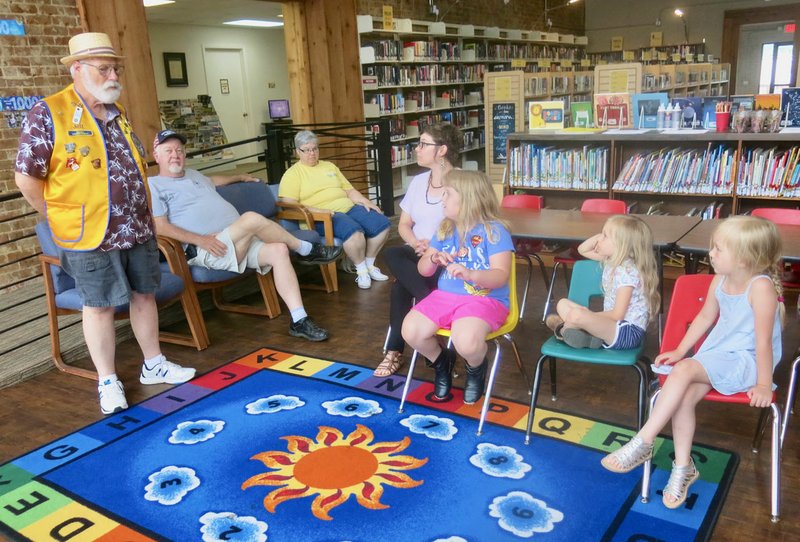 Westside Eagle Observer/SUSAN HOLLAND Jeff Davis (left), secretary of the Gravette Lions Club, tells children attending Helen Keller Day about the Lions Clubs' sight conservation projects, testing children's eyesight at Glenn Duffy Elementary School and collecting used eyeglasses for shipment to other countries. Also listening during the program at the library June 4 are Al Blair, Lions Club president; Sue Rice, Lions Club member; and Brittany Mangold, library clerk.