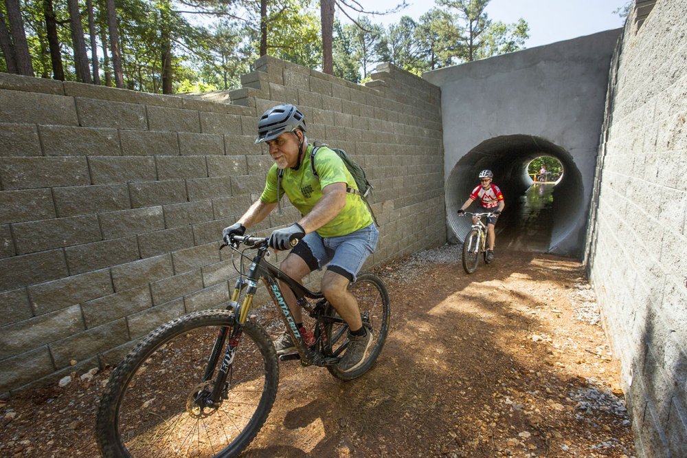 NWA Democrat-Gazette/BEN GOFF @NWABENGOFF Steve Schneider (left) with Rogue Trails leads a group ride, including Patrick Haines of Santiago, Chile, as they pass through the tunnel under Arkansas 12 during the grand opening June 8 of the Monument Trails at Hobbs State Park - Conservation Area near Rogers. The trail is the first in the country, as far as Suzanne Grobmyer's research revealed, to have a soft-surface-to-soft-surface tunnel under a highway as part of the trail system. Grobmyer is the executive director of Arkansas Parks and Recreation Foundation, the nonprofit that developed the new world-class sustainable trails.