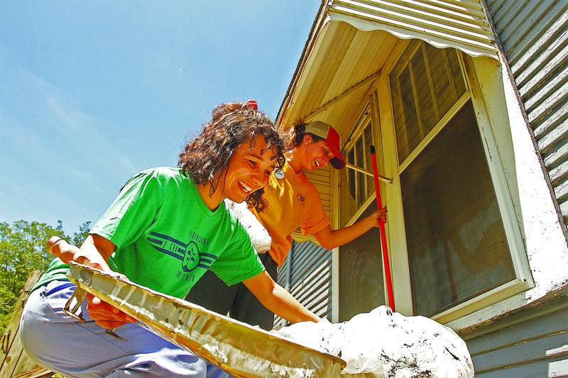 Mission: Ozark Mission Project participants Olivia Myers, left, kneeling, of Siloam Springs and Kinlee Ferguson of Hornbeak, Tennessee clean up after painting a home in El Dorado on Thursday. Terrance Armstard/News-Times