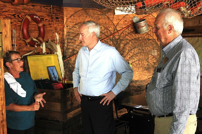 Peggy Hill (left), co-owner of the Triple P Restaurant, describes to Gov. Asa Hutchinson (center) and Desha County’s county judge, Richard Tindall, how customers helped raise the bar, pool table, jukebox and other furniture in the restaurant before it was flooded. 