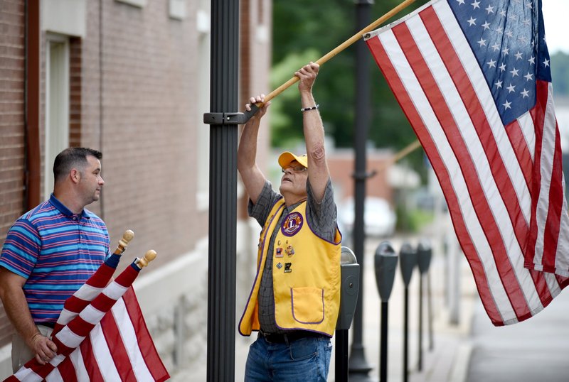 Andrew Aldridge (left) and Steve Gray, both Fayetteville Lions Club members, post Friday a U.S. Flag on a street lamp on the downtown square in Fayetteville in recognition of Flag Day. The installation of the flags on holidays and occasions is a service project for the club and the flags are posted through out the city including Dickson Street, the downtown square and parts of College Avenue. NWA Democrat-Gazette/DAVID GOTTSCHALK