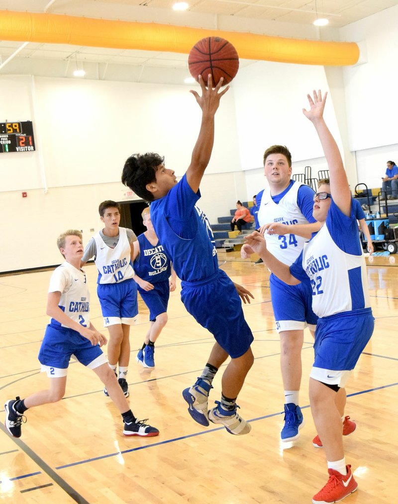 Westside Eagle Observer/MIKE ECKELS Surrounded by Griffin defenders, Decatur's Jose Rubi (center) slides sideways through the air on his way to the basket during game five of the Decatur Summer League scrimmage between Decatur and Ozark Catholic Academy June 11. Decatur emerged the victor in this contest, 33-18, for its second win of the day.