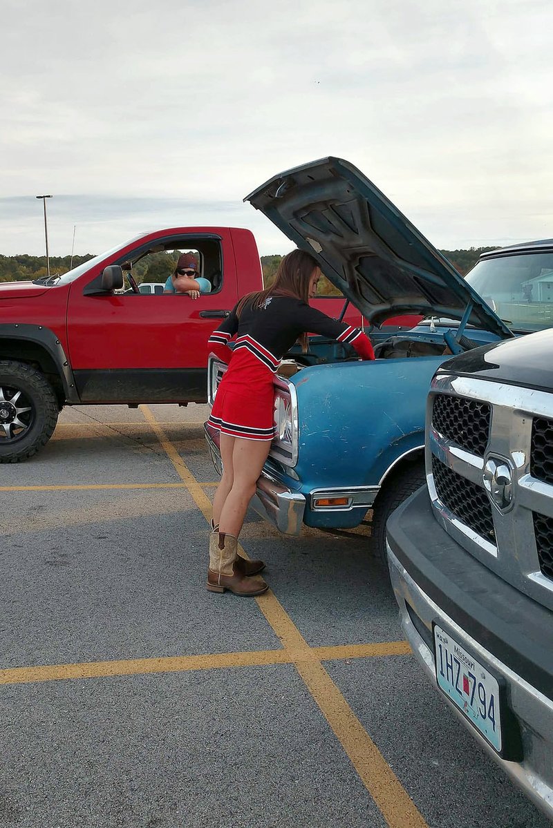 COURTESY PHOTO/Sporting her many hats at once, Paige attaches her alternator wire to start her truck, wearing a cheerleading uniform and cowgirl boots.