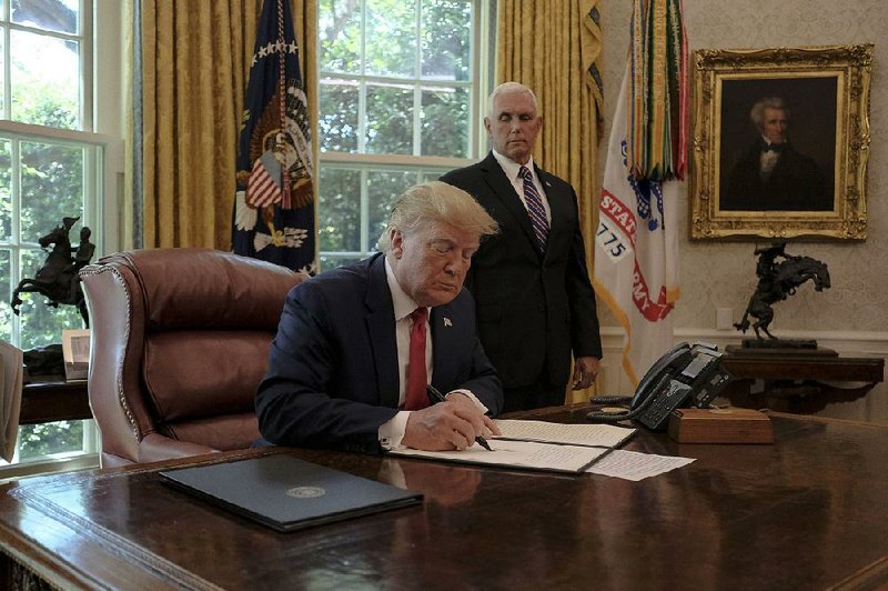 President Donald Trump, joined by Vice President Mike Pence in the Oval Office, signs an executive order Monday to impose more sanctions on Iranians. 