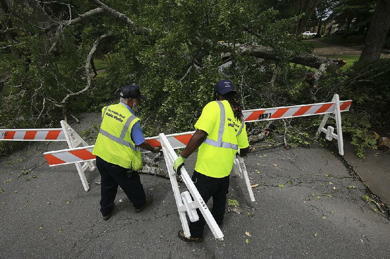 Thomas Robinson (left) and Brandon Cobbs, with the Little Rock Street Department, place barricades Monday afternoon around a tree that fell across Kavanaugh Boulevard near P Street during the latest round of storms. 