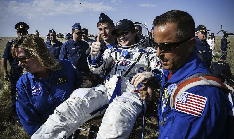 Astronaut Anne McClain, one of  three people who  returned  to  Earth  from the  International Space Station on Tuesday, gives  a thumbs-up while NASA specialists carry her from the landing  site in Kazakhstan. 