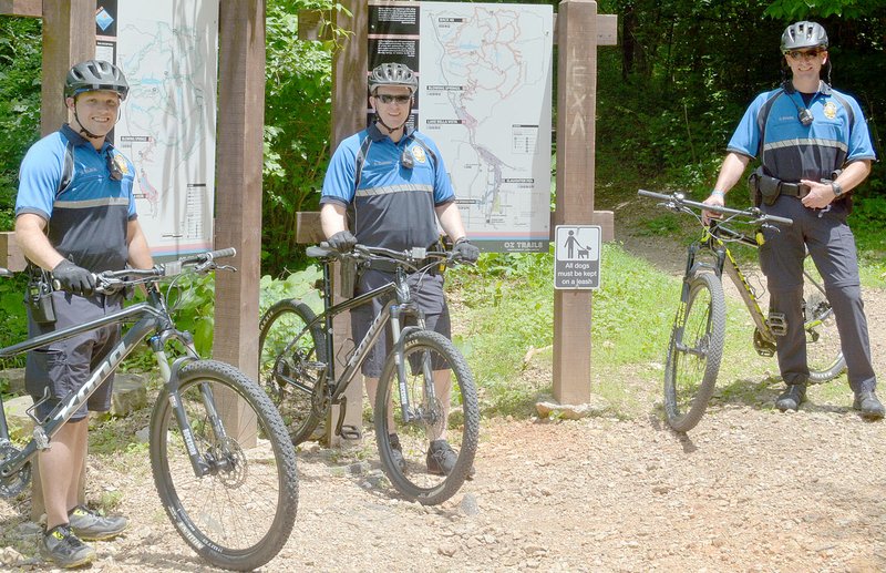 Keith Bryant/The Weekly Vista Bella Vista police officer VJ Wilson (left) stands with Cpl. Bobby Warren and officer Cole Byars near the Back 40 entrance at Blowing Springs. The three officers all serve on the bike patrol unit and spend time monitoring the trails outside their normal shifts.