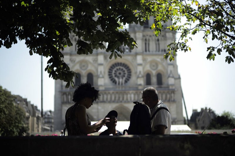 Tourists chat under a tree in front of Notre Dame Cathedral, Wednesday, June 26, 2019 in Paris. High temperatures are expected to go up to 102 Fahrenheit in the Paris area later this week and bake much of the country, from the Pyrenees in the southwest to the German border in the northeast. (AP Photo/Kamil Zihnioglu)