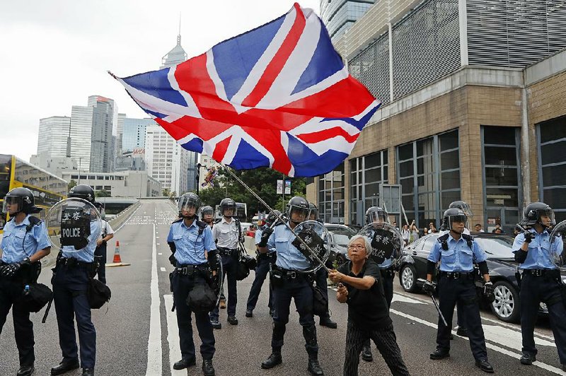 A woman waves a British flag as policemen in anti-riot gear stand guard against protesters on a closed-off road near the Legislative Council in Hong Kong recently. 