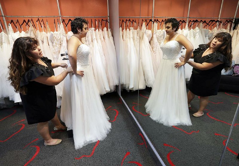 Ann Campeau (left), owner of Strut Bridal, fits a new dress on inventory manager Stefanie Zuniga at her shop in Tempe, Ariz., recently. 