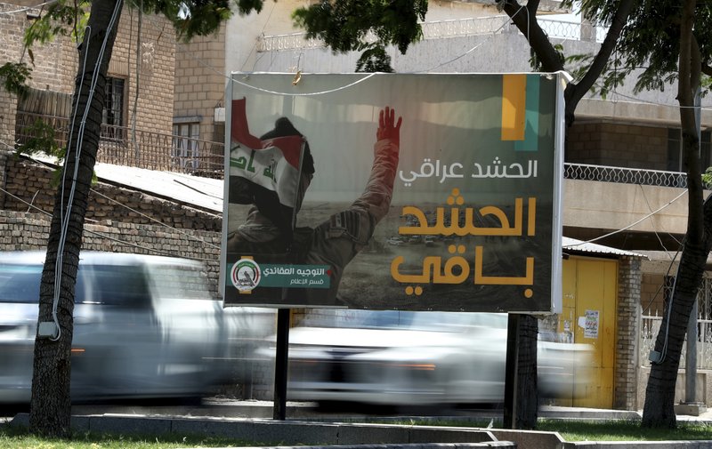 In this Tuesday, July 2, 2019 photo, motorists pass by a Popular Mobilization poster in Baghdad, Iraq. The Iraqi government's move to place Iranian-backed militias under the command of the armed forces is a political gamble by a prime minister increasingly caught in the middle of a dangerous rivalry between Iran and the U.S., the two main power brokers in Iraq. Facing pressure from the U.S. to curb the militias, the move allows Prime Minister Adel Abdul-Mahdi to portray a tough stance ahead of a planned visit to Washington. It is unlikely, though, that he would be able to rein in and neutralize Iran-supported groups and he risks coming off as a weak and ineffective leader if he doesn't. The Arabic sentence on the poster reads, &quot;the Popular Mobilization is Iraqi and will last.&quot; (AP Photo/Hadi Mizban)