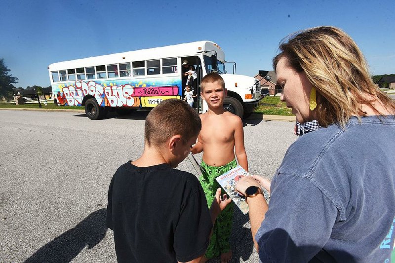 Holly Elsea, a  teacher at Creekside Middle School  in Centerton, checks out the books some children selected from the Bridge Bus traveling library. 