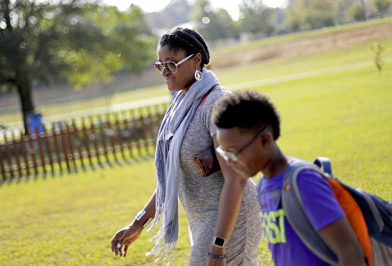 In this Oct. 11, 2017 file photo, Corrie Davis, left, picks up her son Turner from Big Shanty Elementary School in Kennesaw, Ga. The previous month, the school invited fifth-graders to dress up as characters from the Civil War. Davis says a white student dressed as a plantation owner approached her son and said "You are my slave." She requested that the school to stop the annual Civil War dress-up day. Recently, an investigation by New York Attorney General Letitia James found in May that a mock "slave auction" that singled out black students at the private Chapel School in Westchester County had a profoundly negative effect on all involved students. (AP Photo/David Goldman, File)