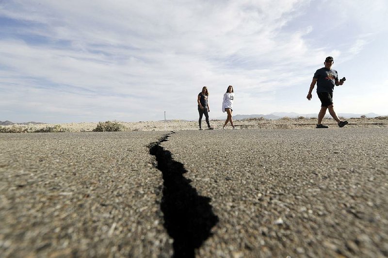 People walk next to a crack in the road Sunday caused by an earthquake as they cross California 178 near Ridgecrest. 