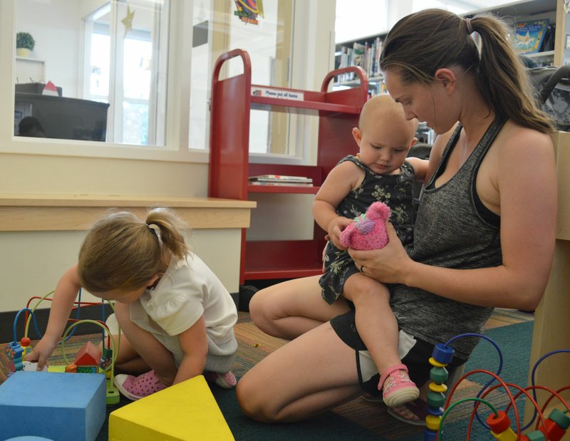 Sierra Bush/Herald-Leader Amanda Oliva (right) plays with her daughter, Elizabeth, while her other daughter, Evelyn, engages with blocks at the Siloam Springs Public Library. The Oliva girls participate in the summer reading program and go to the library frequently to read after their nap times.