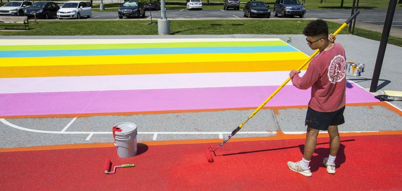NWA Democrat-Gazette FILE PHOTO/BEN GOFF Dominick Griggs, a junior at Bentonville West High School, helps paint a mural Wednesday, May 15, 2019, on the basketball courts at Memorial Park in Bentonville. The mural with a 1970's theme was designed by Bentonville High senior Jonathon Coppick and is included in the city's art map.