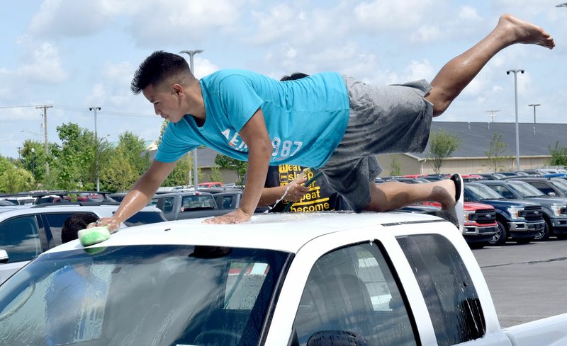 Westside Eagle Observer/MIKE ECKELS Looking more like a classic Ford hood ornament, Kevin Sanchez cleans the corner of the roof of a pickup during the July 9 Decatur Bulldog cheer team's carwash in Bentonville.