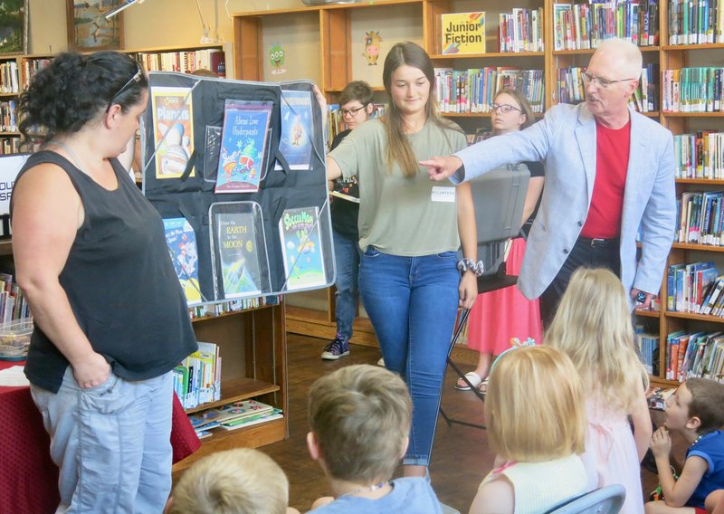 Westside Eagle Observer/SUSAN HOLLAND
Magician Alan Burdick, from Lowell, points out books about space exploration during his presentation Tuesday, July 9, at the Gravette Public Library. Burdick's magic show was a popular feature of the library's "Mission Accomplished" celebration at the close of the children's summer reading program. Assisting with the program are library volunteers Audrey Ratledge and Katie Trimble. story.lead_photo.caption
