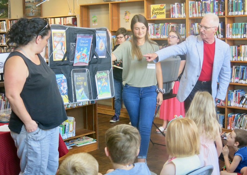 Westside Eagle Observer/SUSAN HOLLAND
Magician Alan Burdick, from Lowell, points out books about space exploration during his presentation Tuesday, July 9, at the Gravette Public Library. Burdick's magic show was a popular feature of the library's "Mission Accomplished" celebration at the close of the children's summer reading program. Assisting with the program are library volunteers Audrey Ratledge and Katie Trimble.      