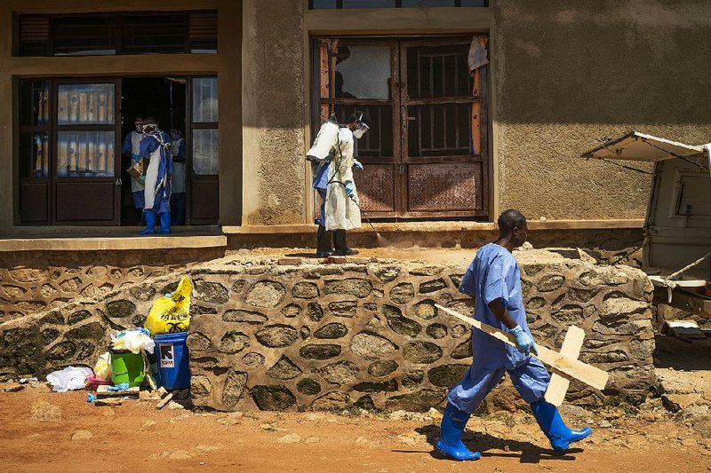 A morgue employee carries a cross Sunday past others disinfecting the entrance to the morgue in Beni, Democratic Republic of Congo. A recent ebola outbreak has killed more than 1,500 people in that country. 