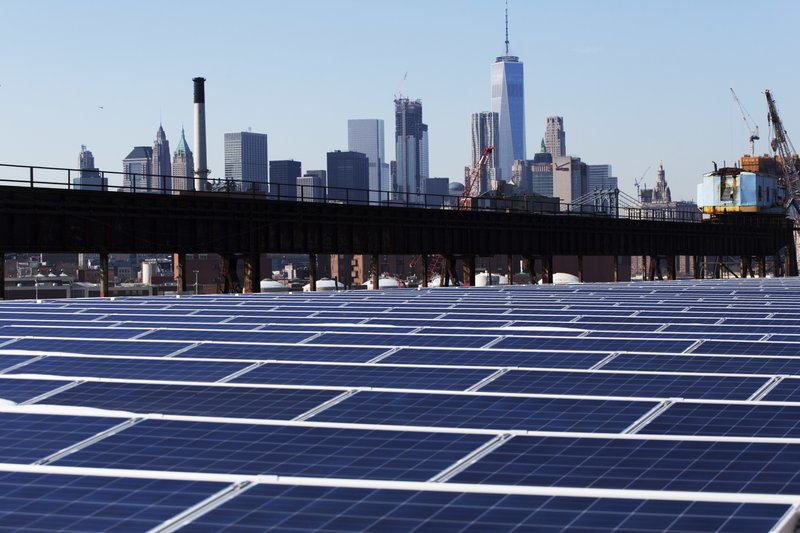 FILE - In this Feb. 14, 2017, file photo, a rooftop is covered with solar panels at the Brooklyn Navy Yard in New York. The Manhattan skyline is at top. A new law signed Thursday by New York Gov. Andrew Cuomo sets the nation's most aggressive targets for reducing carbon emissions and is intended to drive dramatic changes over the next 30 years. It calls for all the state's electricity to come from renewable, carbon-free sources such as solar, wind and hydropower. Transportation and building heating systems would also run on clean electricity rather than oil and gas. (AP Photo/Mark Lennihan, File)
