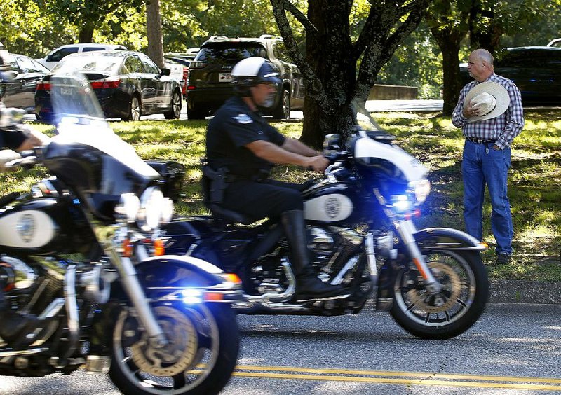 Keith Stokes (right) of Dardanelle pays his respects Friday as the police procession escorting the body of Stone County Deputy Mike Stephen leaves the state Crime Laboratory in Little Rock. 