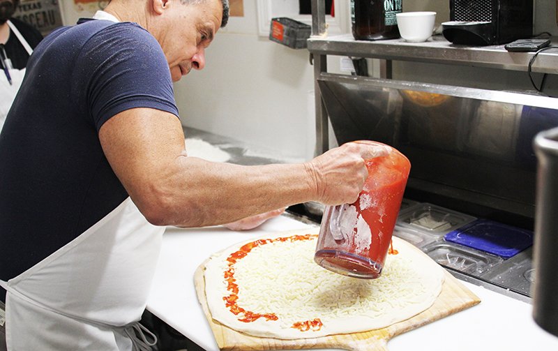 The Sentinel-Record/Tanner Newton MAKING PIZZA: Deluca's Pizzeria owner Anthony Valinoti pours sauce onto a pizza at the restaurant. Valinoti helped the filmmakers of indie movie "Phoenix, Oregon" with tips on how to make pizzas in the film.