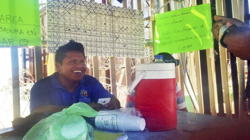 In this July 2, 2019 photo provided by Jesse Tellera, asylum seeker Claudio Aviles sits by a posted list of migrants who are in San Luis Rio Colorado, Mexico, waiting to seek asylum in the United States. Aviles, of Guerrero, Mexico, has since made it to the U.S. with his wife and young children. (Jesse Tellera via AP)