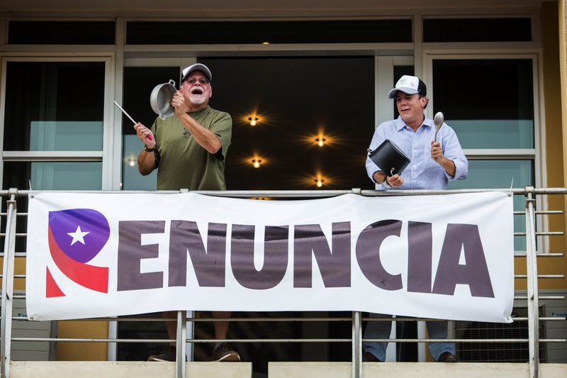 Demonstrators bang on pots, from the balcony of their apartment as they protest against governor Ricardo Rossello, in San Juan, Puerto Rico, Friday, July 19, 2019. Protesters are demanding Rossello step down for his involvement in a private chat in which he used profanities to describe an ex-New York City councilwoman and a federal control board overseeing the island's finance. (AP Photo/Dennis M. Rivera Pichardoi)